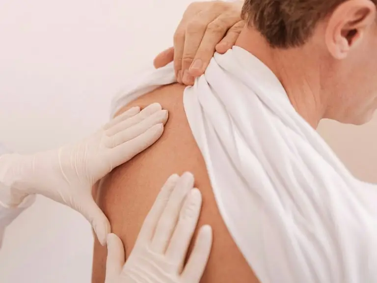 Hautarzt mit weißen Handschuhen untersucht den Rücken eines Patienten